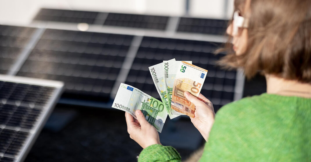 Frau hält Euro-Scheine vor Solarpanele als Zeichen für Photovoltaik-Einsparungen