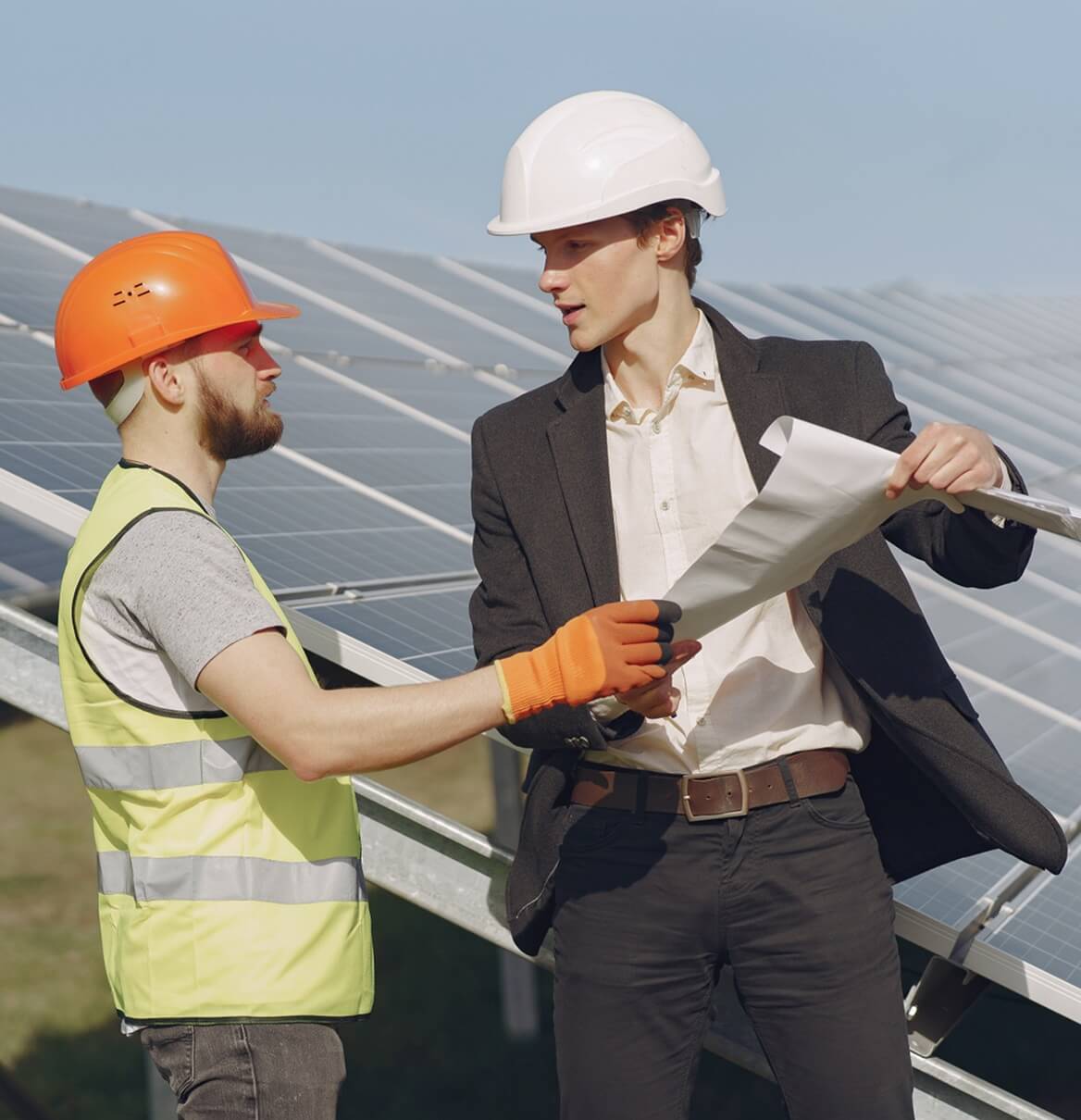 Elektriker und Planer besprechen Baupläne vor Solaranlage auf Freigelände