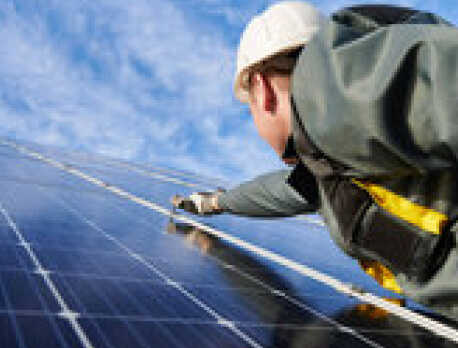Elektriker mit Schutzhelm arbeitet mit Werkzeug an Photovoltaikmodul auf Dach